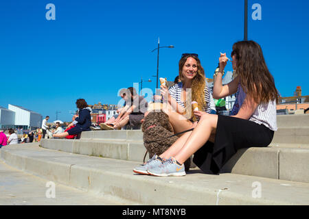 Due donne e un cane seduto di fronte spiaggia a Margate, mangiare il gelato e parlare, Margate, Regno Unito Foto Stock