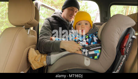 Papà unfastens cinghie sedile e ascensori figlio su auto Foto Stock