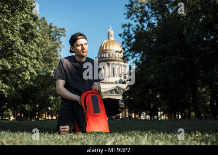 Youg uomo turistico con zaino udienza del picnic su erba, vicino a Cattedrale di San Isacco in San Pietroburgo nella soleggiata giornata estiva. Foto Stock