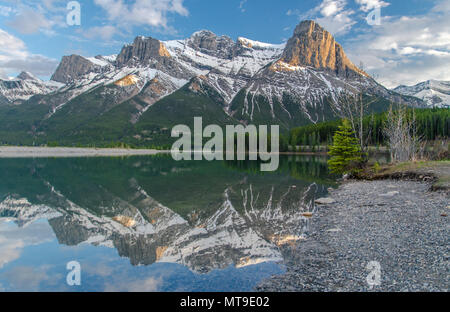 Montagne innevate, le tre sorelle, perfettamente riflessa in Canmore serbatoio al tramonto, cielo dipinto con gli ultimi raggi solari. Alberi e acqua. Foto Stock