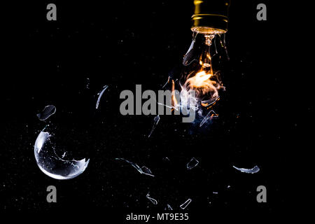 Una lampadina in frantumi mentre illuminato con fiamme e fumo e azione di arresto sul vetro in frantumi Foto Stock