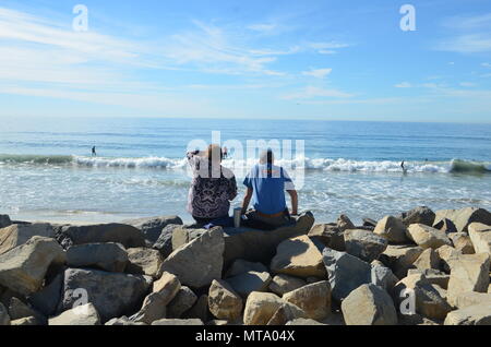 Carlsbad State Beach. Giovane seduto su rocce di grandi dimensioni, guardando i surfisti. Foto Stock