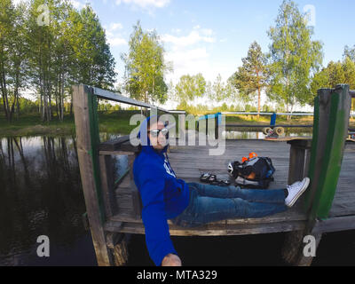 Il giovane fa un selfie seduta sul molo in riva al lago Foto Stock