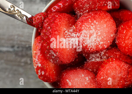 Vista dall'alto in dettaglio su una piccola ciotola con fresche fragole tagliate cosparso con cristallo bianco zucchero, cucchiaio d'argento suggerendo che sono pronti a mangiare. Foto Stock