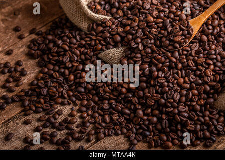 Al di sopra del sacco versato del caffè fresco fagioli con il cucchiaio di legno Foto Stock