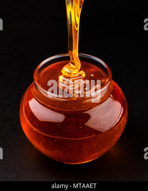 Pentola di colata di miele su sfondo nero Foto Stock