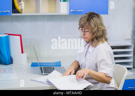 Felice medico senior con appunti alla ricezione dell'ospedale Foto Stock