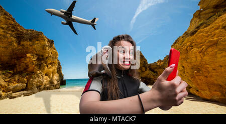 Bella femmina windsurfer sportman in mute con il telefono sulla spiaggia, scimmia seduto sulla sua spalla, aereo su sfondo Foto Stock