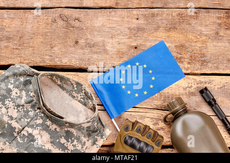 Ue soldato dell'esercito elementi laici piana. Blue bandiera europea e cose militari sul tavolo di legno con copyspace. Foto Stock