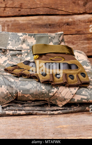 Camouflage abiti militari e guanti senza dita. Immagine ritagliata. In legno marrone sfondo scrivania. Foto Stock