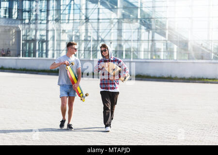 Due amici del ragazzo in occhiali da sole azienda skateboard longboard e camminare prima di edificio moderno Foto Stock