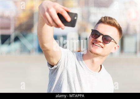 Guidatore di skateboard rende selfie prima di edificio moderno in giornata di sole Foto Stock