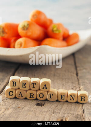 Dadi di legno con le parole il beta-carotene e le carote fresche nel retro, mangiare sano concetto Foto Stock