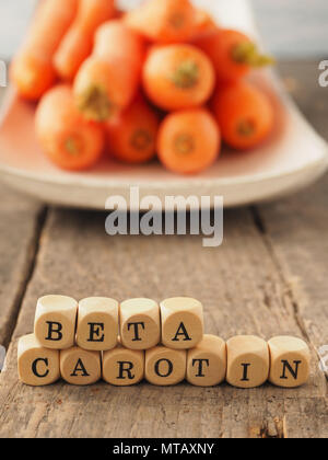 Dadi di legno con le parole tedesche il beta-carotene e le carote fresche nel retro, mangiare sano concetto Foto Stock