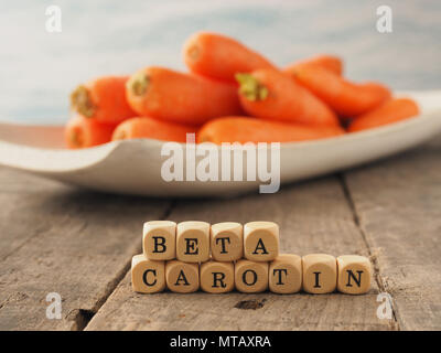 Dadi di legno con le parole tedesche il beta-carotene e le carote fresche nel retro, mangiare sano concetto Foto Stock