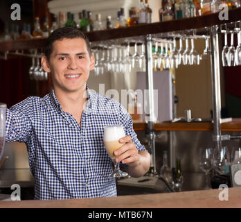 Sorridente bello barista in piedi dietro il bancone bar e h Foto Stock