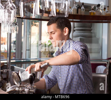 Bel giovane barista dietro il bancone bar in acciaio azienda ic Foto Stock