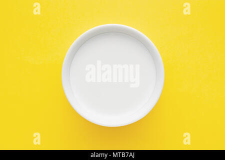 Top down vista minimalista di latte in un recipiente bianco su sfondo giallo Foto Stock