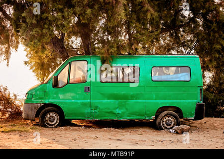 Rottami abbandonati green mini van con un pneumatico sgonfio vicino al mare Foto Stock