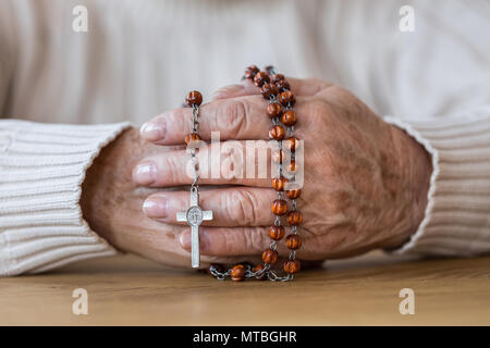 Close-up di senior le mani tenendo un rosario rosso con croce d'argento Foto Stock