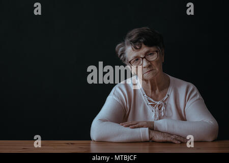 Triste, anziani donna sola seduta accanto a tabella Foto Stock