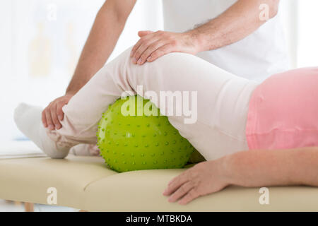 Senior paziente in fase di riabilitazione in un ospedale con un massaggio verde palla sotto la sua gamba sinistra Foto Stock