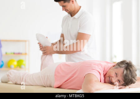 Fisioterapista applicando sollievo muscolare esercizi per una donna senior della gamba Foto Stock