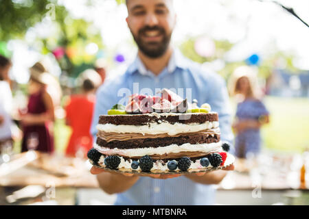 Uomo con una torta su una festa in famiglia o un party in giardino esterno. Foto Stock