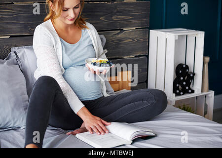 Donna incinta di mangiare e la lettura di un libro Foto Stock