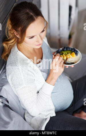 Donna incinta di fare colazione in camera da letto Foto Stock