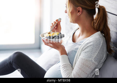 Vista laterale della donna incinta di fare colazione in camera da letto Foto Stock