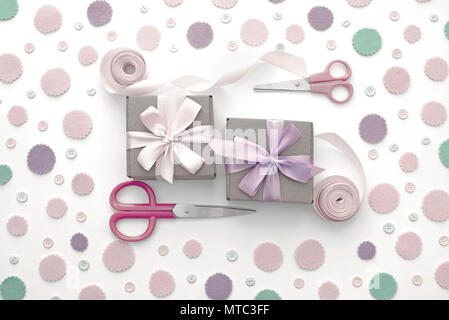 Due confezioni regalo sul pastello festosa coriandoli sfondo. Regali Imballaggio in scatole di Kraft con un nastro di raso bow forbici. Appartamento laici vista superiore Foto Stock