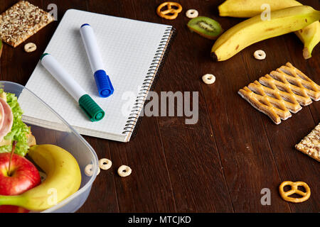 Un notebook, due marcatori e assortimento di biscotti su di un tavolo di legno, copiare lo spazio per testo, il fuoco selettivo. Scuola di concetto di pranzo. Nutriente merenda per Foto Stock