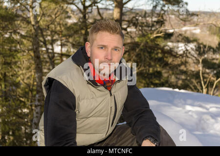 Ritratto di metà adulto 40s uomo caucasico seduti all'aperto nella neve in inverno guardando sorridente della fotocamera Foto Stock