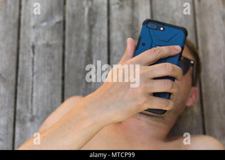 Barechested metà adulto 40s uomo caucasico utilizza lo smartphone telefono cellulare all'aperto sul patio quando vi rilassate in sun Foto Stock