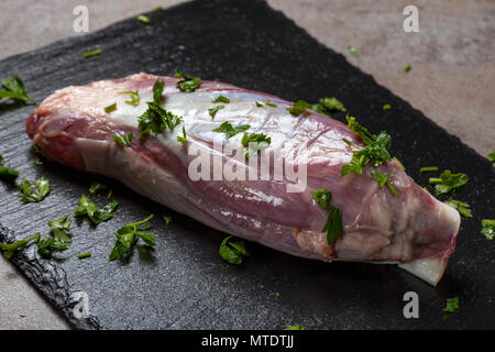 Un nuovo pezzo grezzo della carne di manzo fresco con prezzemolo verde su un di ardesia scura Foto Stock