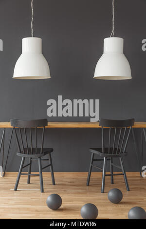 Sedie nere al tavolo di legno sotto le lampade bianche in sala da pranzo interno con sfere Foto Stock