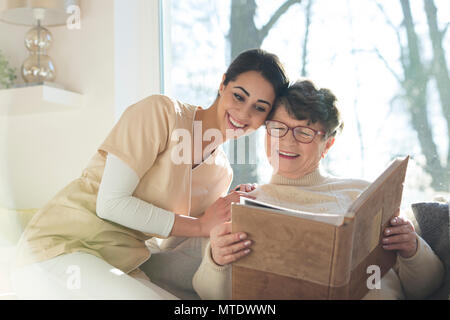 Geriatrico paziente con demenza insieme con una riabilitazione professionale infermiera guardando un album di foto di famiglia in un privato assisted living home Foto Stock