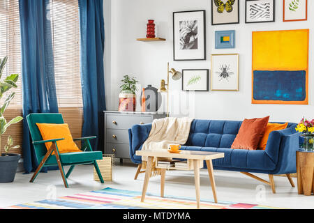 Foto reale di un colorato soggiorno interno con una poltrona verde e blu navy divano in piedi in un tavolo da caffè in legno Foto Stock