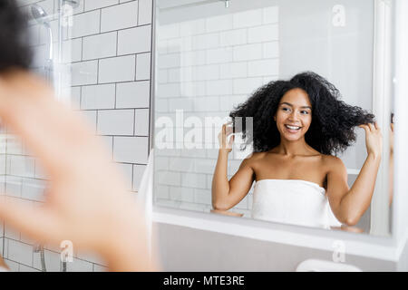 Giovane donna prendendo la decisione su un'acconciatura davanti a uno specchio Foto Stock