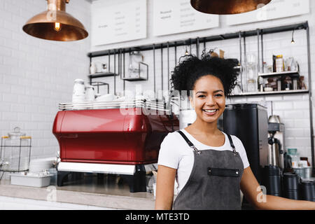 Felice giovane barista in piedi in cafe indossando il grembiule Foto Stock