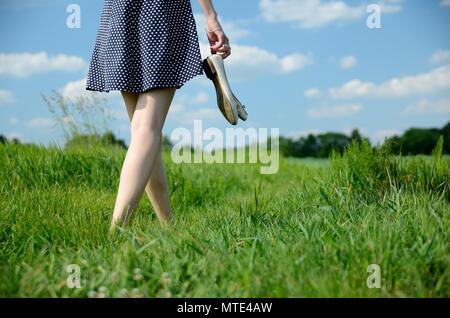 Passeggiate femmina sull'erba a piedi nudi. Giovane donna gode di outdoor a piedi, natura, campi verdi e blu del cielo. Foto Stock