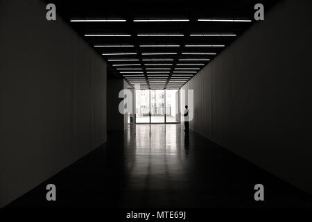 Una persona in piedi in corridoi bui con porte francesi che lasciano la luce alla fine nella galleria a cubo bianco a Bermondsey, Londra Foto Stock