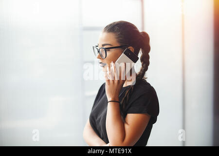 Bruna giovane ragazza con gli occhiali parla al telefono cellulare Foto Stock