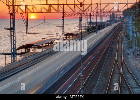 Vista aerea della stazione ferroviaria con moto treno sfocata sullo sfondo del mare al tramonto, Sochi, Russia Foto Stock