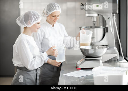 Due femmina pasticceri in uniforme del peso di ingredienti per pasticceria lavorando presso la pasticceria La fabbricazione Foto Stock