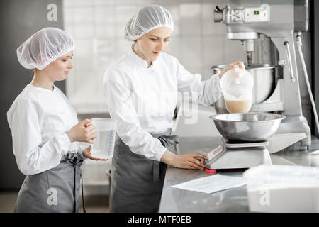 Due femmina pasticceri in uniforme del peso di ingredienti per pasticceria lavorando presso la pasticceria La fabbricazione Foto Stock