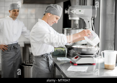 Due maschi bello pasticceri in uniforme del peso di ingredienti per la cottura a livello di fabbricazione Foto Stock