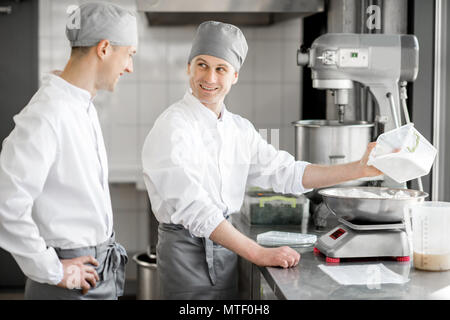 Due maschi bello pasticceri in uniforme del peso di ingredienti per la cottura a livello di fabbricazione Foto Stock