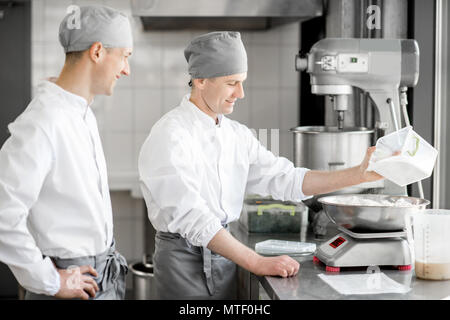 Due maschi bello pasticceri in uniforme del peso di ingredienti per la cottura a livello di fabbricazione Foto Stock